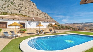 A swimming pool with lounge chairs and umbrellas, surrounded by a white building with a stone facade, set against a mountainous backdrop. - Casa Maria Caminito del Rey Valle de Abdalajís by Ruralidays (Province of Málaga)