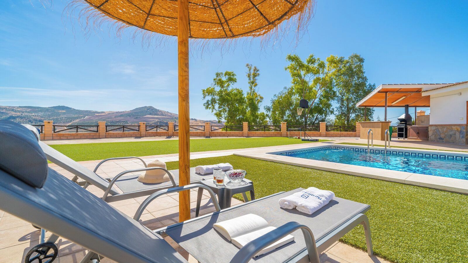 A poolside area with lounge chairs, a table with towels, and a view of the pool and mountains.