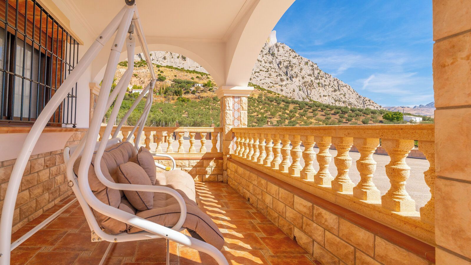 A balcony with a hanging chair, stone balustrade, and a view of a mountainous landscape.