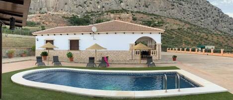 Une maison avec une piscine, un espace salon extérieur et un paysage montagneux en toile de fond.