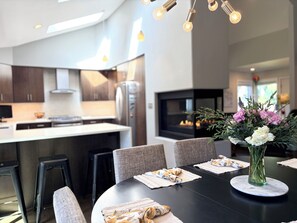 Ett modernt kök med en central köksö, ett matbord med stolar och en vas med blommor.