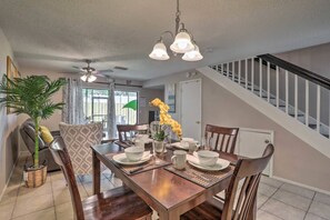 A dining area with a wooden table set for four, a ceiling fan, and a staircase with white railings. - Near Tampa, St. Pete & Top Beaches + Pet-Friendly! (Largo)