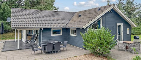 A two-story house with a covered patio, outdoor furniture, and a small garden area.