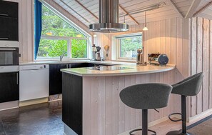 Una cocina moderna con una isla central, taburetes de bar, un lavavajillas Bosch y un ventanal con vistas a zonas verdes.