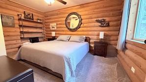 Ein Schlafzimmer in einer Blockhütte mit einem Bett, Nachttischen, einem Spiegel und Wanddekorationen.