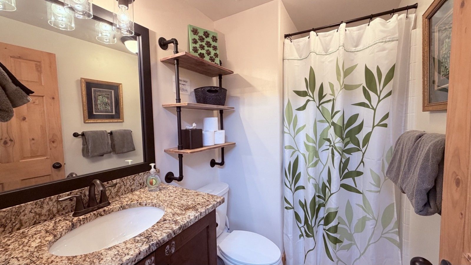 Un bagno con lavabo in granito, wc e tenda da doccia con motivo a foglia.