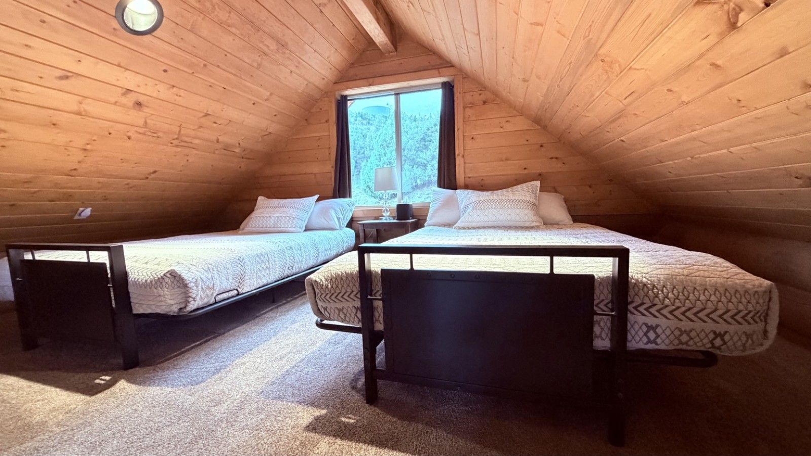 Una camera con due letti, una finestra e un soffitto in legno.