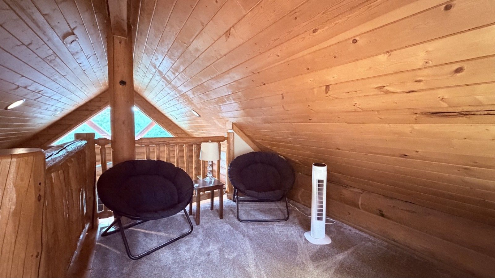 A wooden cabin room with a sloped ceiling, two black chairs, a small table, and a white heater.