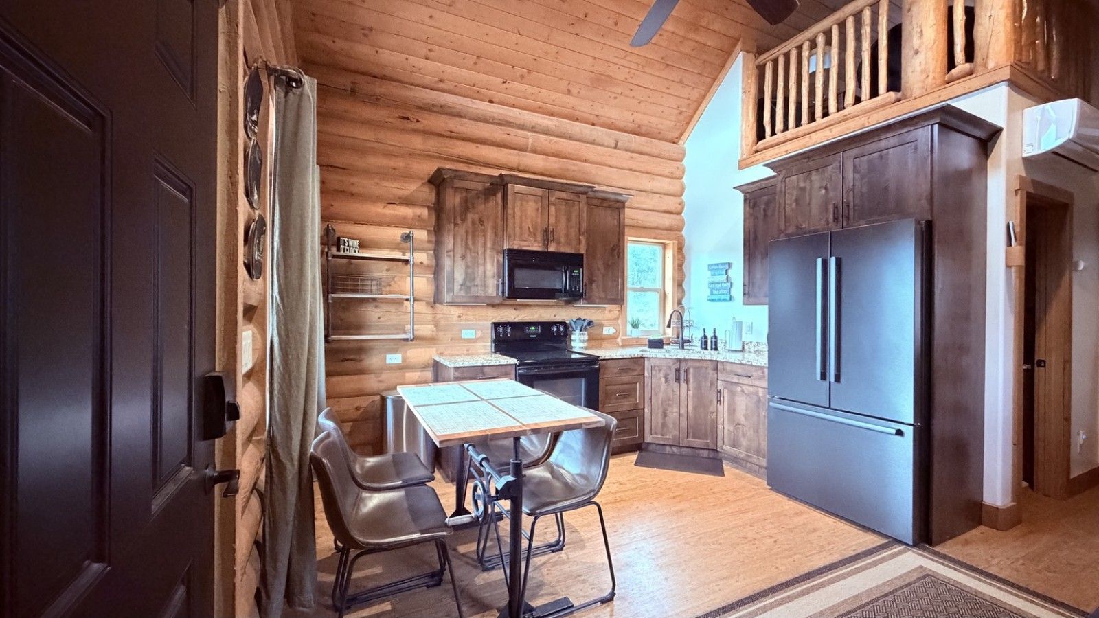 A wooden interior with a kitchen area featuring a dining table, chairs, a refrigerator, and a microwave.