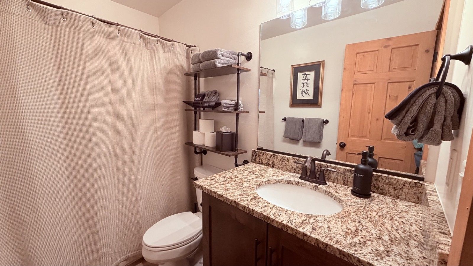 A bathroom with a shower curtain, a toilet, a sink with a marble countertop, a mirror, and a towel rack.
