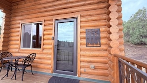 Eine Blockhütte mit einer Holzterrasse, einer Tür und einem Schild mit Koordinaten und Höhenangabe.