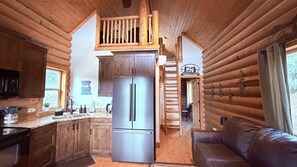Interior de uma cabana de tronco com cozinha, área de jantar e sala de estar.