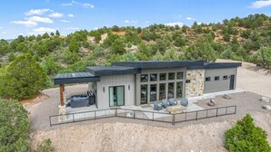 A modern two-story house with a patio area, large windows, and a stone facade. - Bryce Gateway Retreat — 2BR Cabin with Hot Tub & Mountain Views, Between Bryce & Zion (Alton)