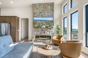 A modern living room with a stone fireplace, a large flat-screen TV, and a view of a mountainous landscape.