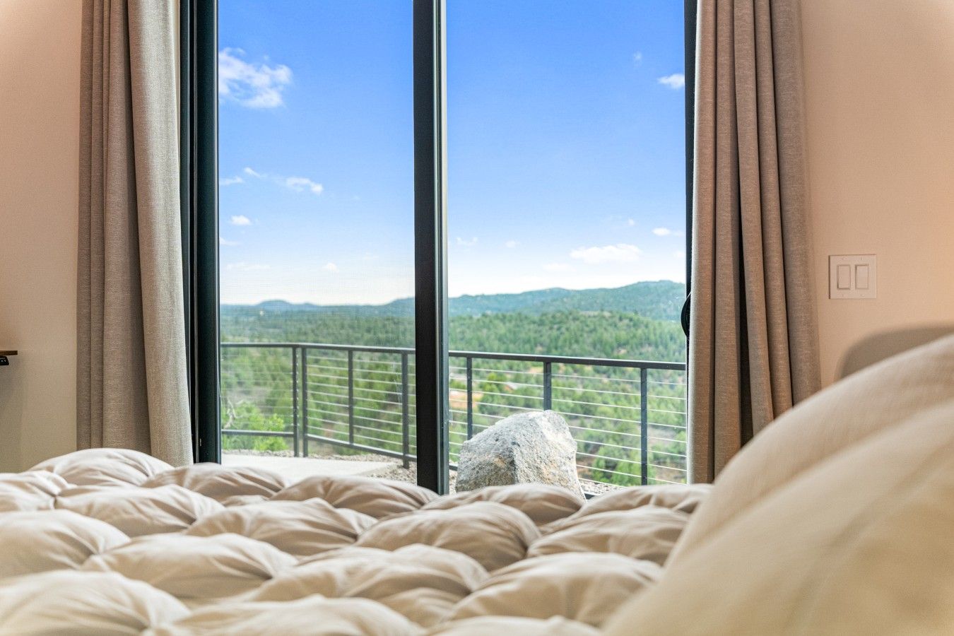 Una camera d'hotel con un letto grande, vista su un balcone con ringhiera e un paesaggio montano sullo sfondo.