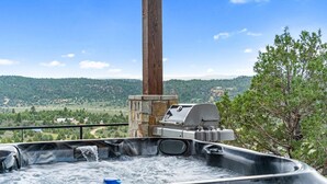 A hot tub with a stone structure and grill, overlooking a scenic landscape. - Bryce Gateway Retreat — 2BR Cabin with Hot Tub & Mountain Views, Between Bryce & Zion (Alton)