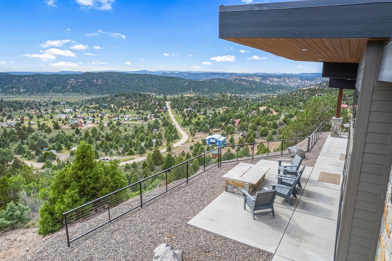 A balcony with a view of a rural landscape, outdoor seating, and a stone fireplace.