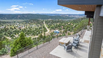 A balcony with a view of a rural landscape, outdoor seating, and a stone fireplace.