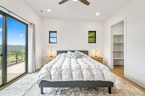Quarto com uma cama grande, duas mesas de cabeceira, um ventilador de teto e vista para o exterior.
