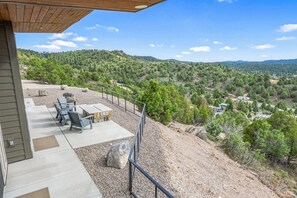 Um pátio com móveis de exterior, vista para uma paisagem montanhosa e céu limpo.