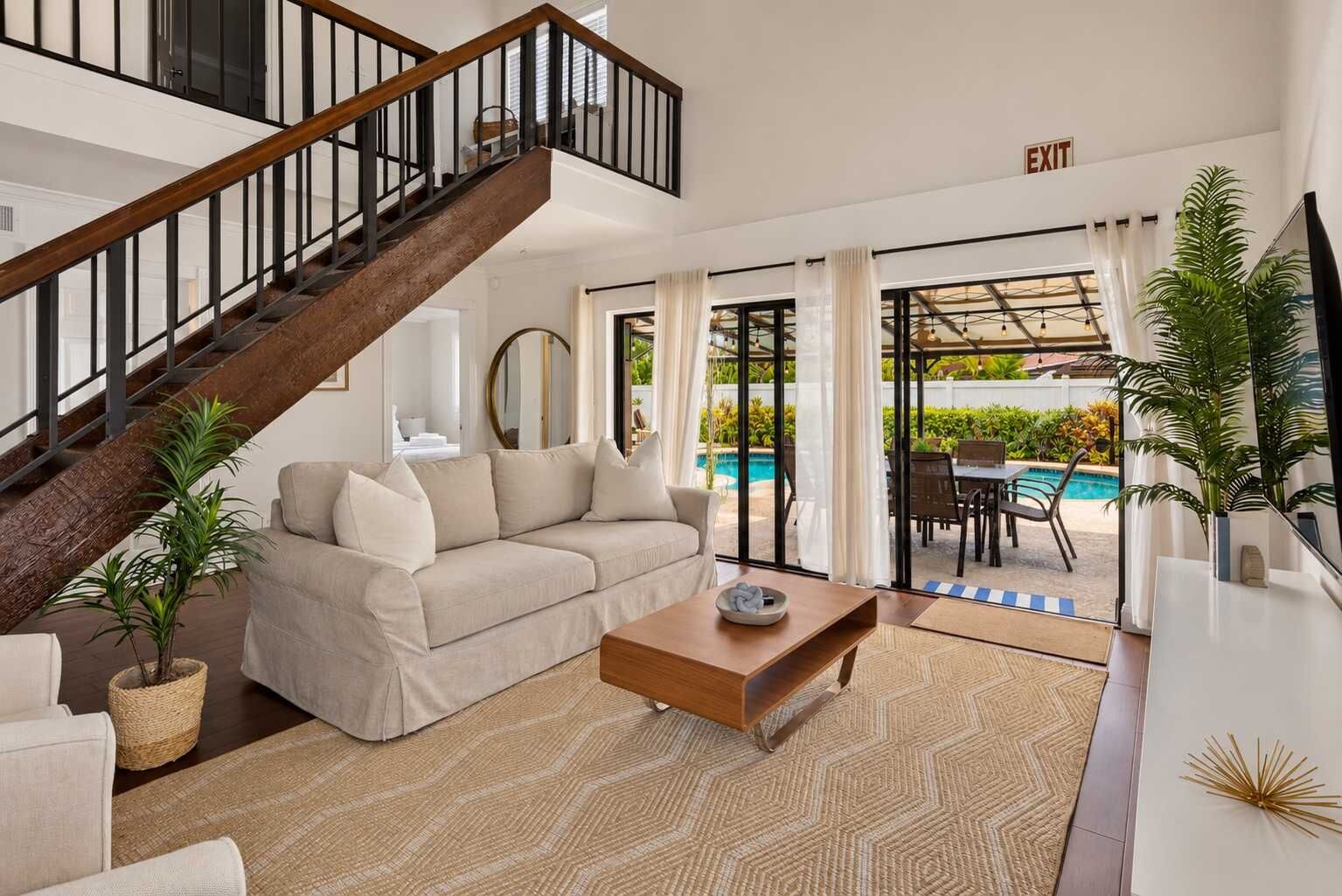 Ein modernes Wohnzimmer mit Treppe, einer Couch, einem Couchtisch und Blick auf einen Poolbereich im Freien.