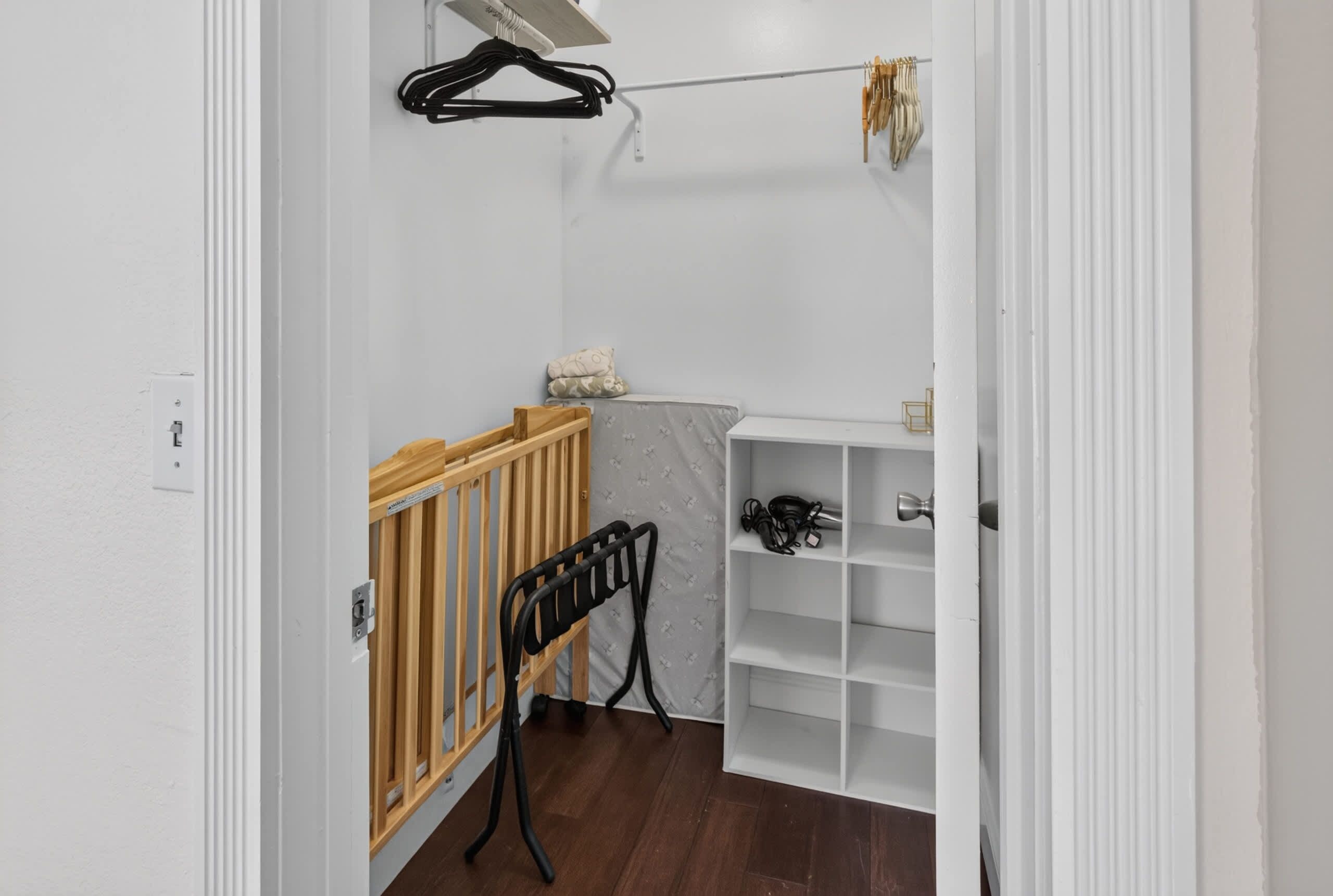 Een kamer met een houten ledikant, een witte plankkast en een kledingrek met kleren.