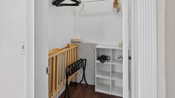 Een kamer met een houten ledikant, een witte plankkast en een kledingrek met kleren.