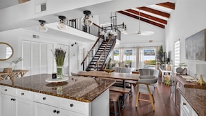 A spacious kitchen with a large island, a dining area with a wooden table, and a staircase leading to an upper level. - Navigate Stays Delray Beach, FL, Pool - Near Beach (Delray Beach)