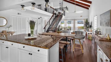 Eine großzügige Küche mit einer großen Kochinsel, ein Essbereich mit einem Holztisch und eine Treppe, die in ein Obergeschoss führt.
