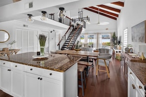 A spacious kitchen with a large island, a dining area with a wooden table, and a staircase leading to an upper level.