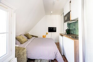 A compact bedroom with a bed, a nightstand, a TV, and a kitchenette. - Maraisette - Métro - 4ème arrondissement (Paris)