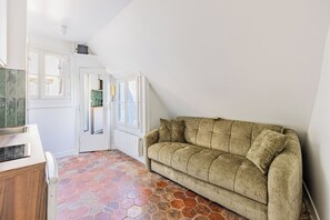 A room with a stone-patterned floor, a beige sofa, and white walls. - Maraisette - Métro - 4ème arrondissement (Paris)