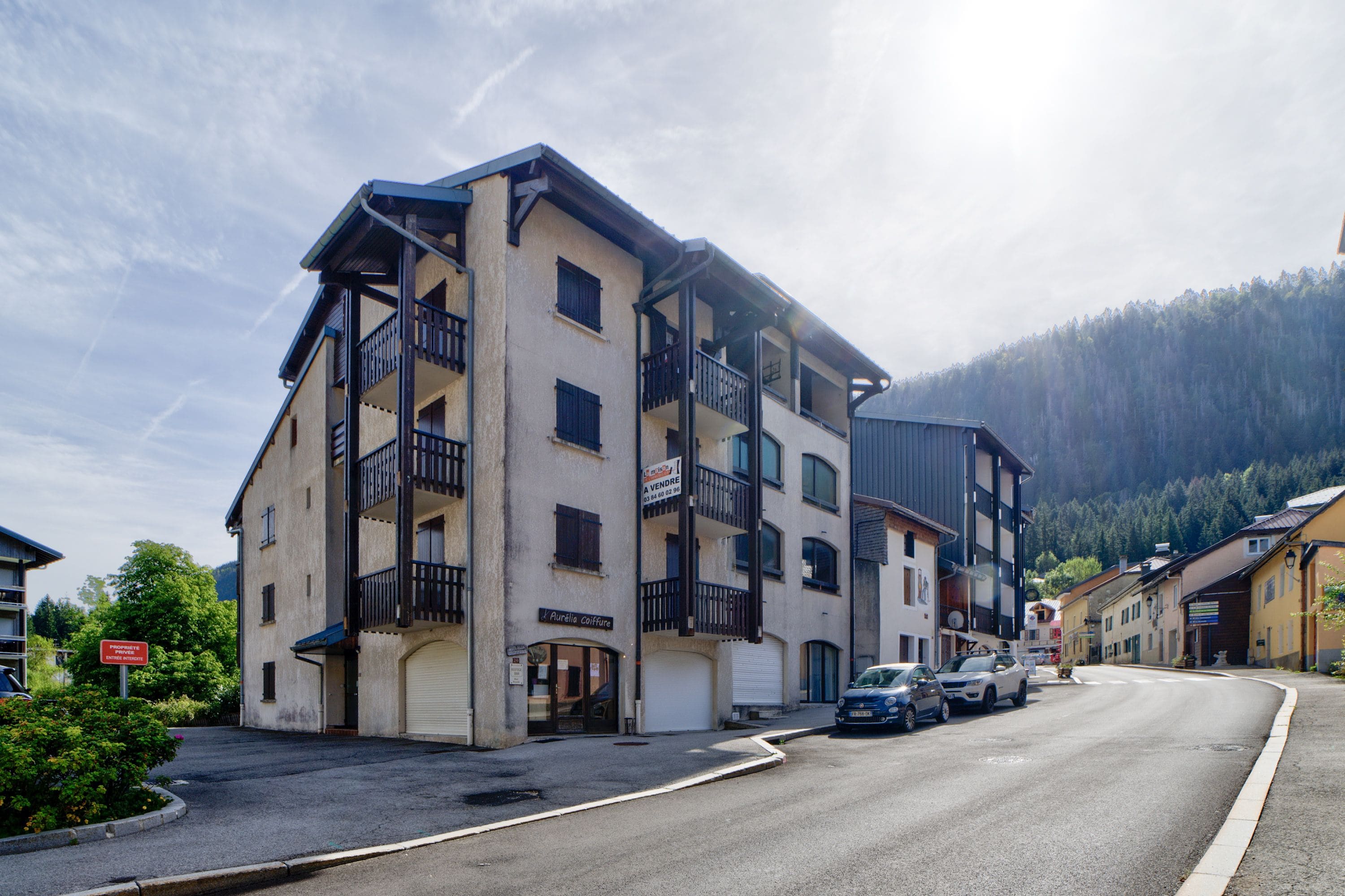 Un immeuble à plusieurs étages doté de balcons, d’une devanture de magasin et de voitures garées dans la rue.