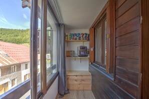 A narrow balcony with wooden railings, a small shelf with books, and a view of a red-roofed building.