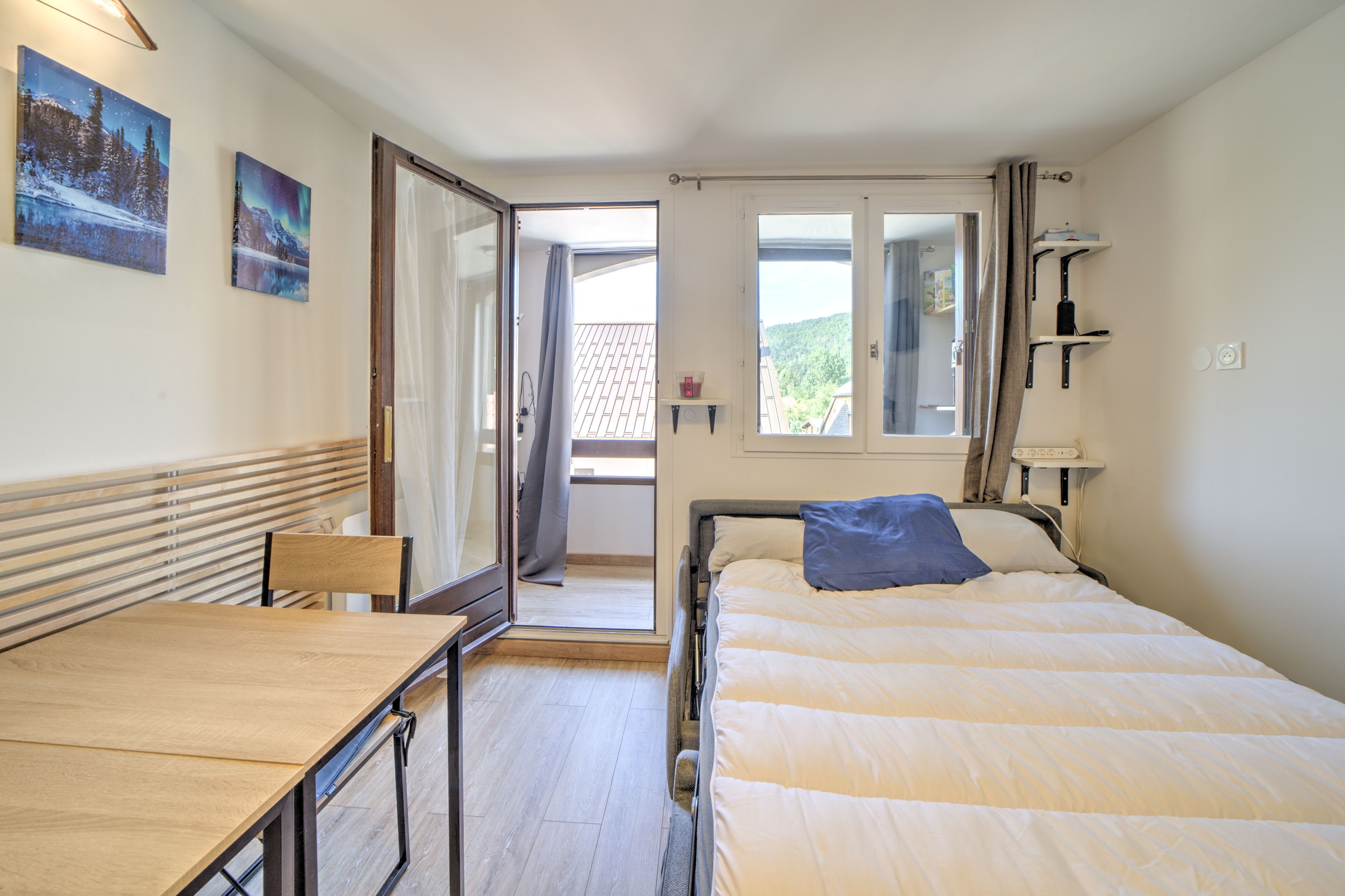 Quarto com cama, escrivaninha e cadeira. Janela com vista para o exterior.