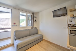 A room with a grey sofa, a television mounted on the wall, and a coffee machine.
