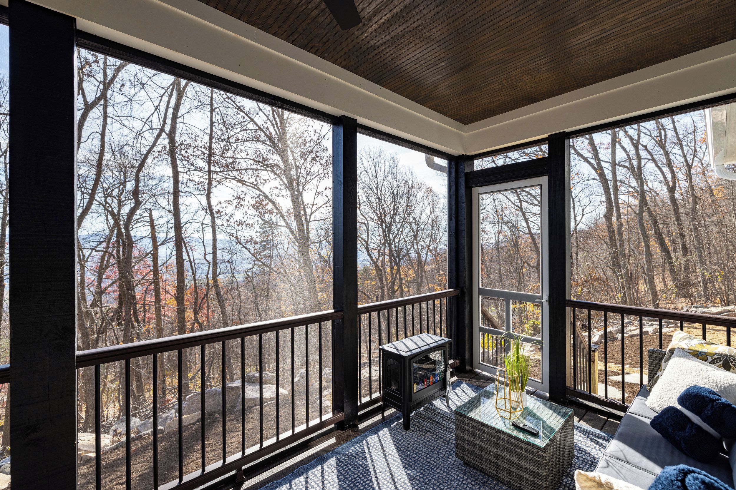 A room with large windows, a balcony, and a view of trees.