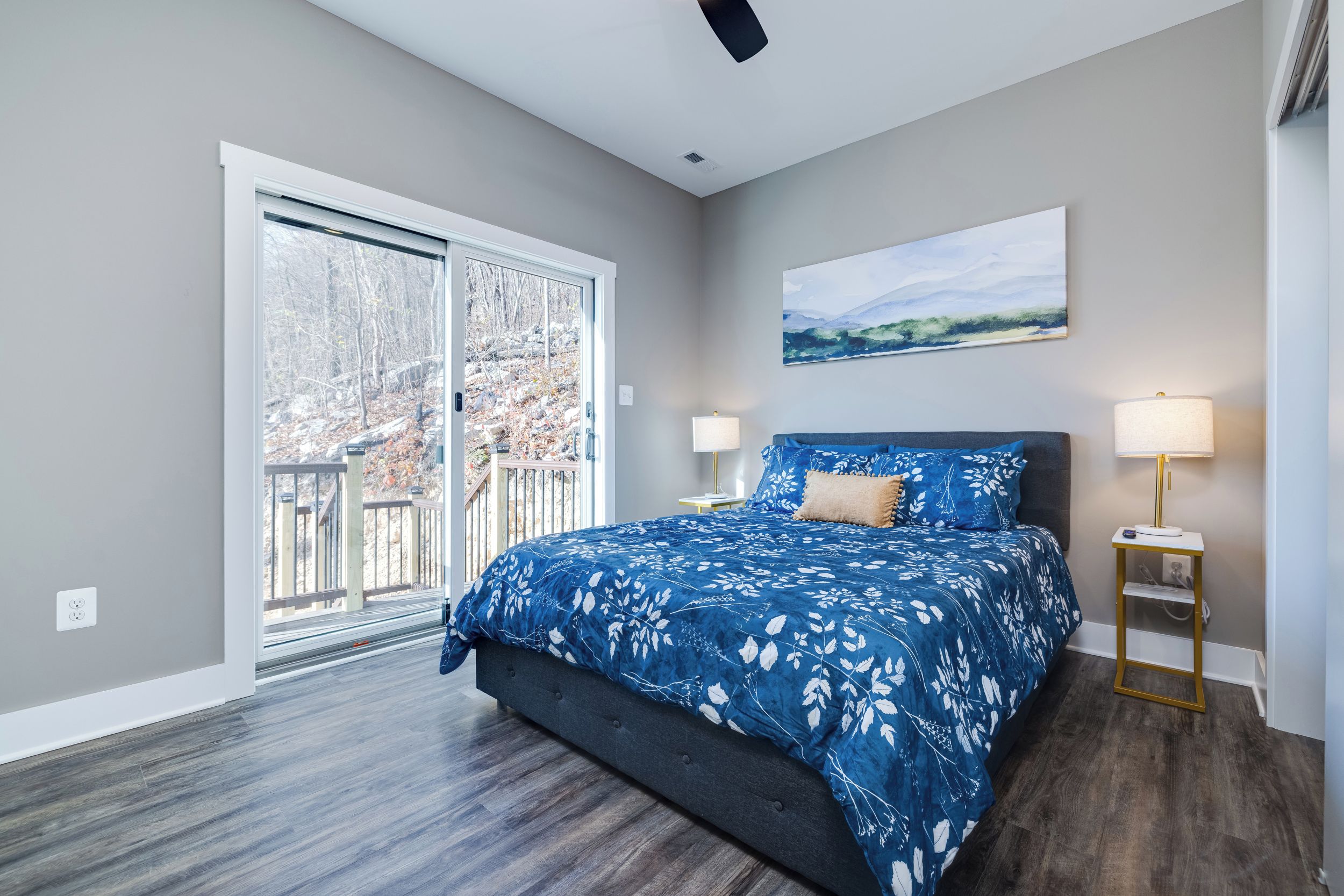 A bedroom with a large bed, a sliding glass door to a balcony, and a painting on the wall.