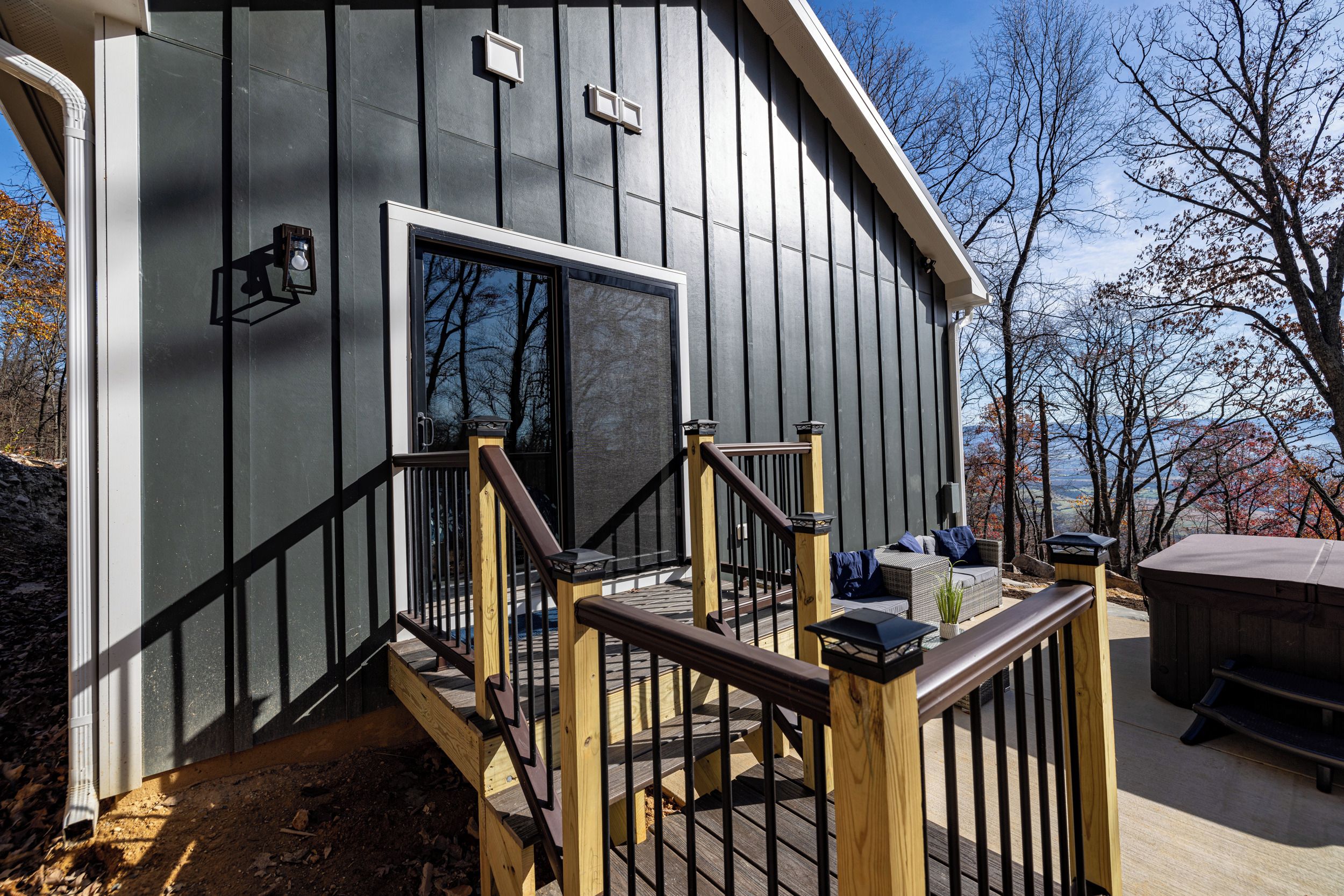 A modern building with a dark exterior, a wooden deck with a railing, and a clear view of the surrounding landscape.