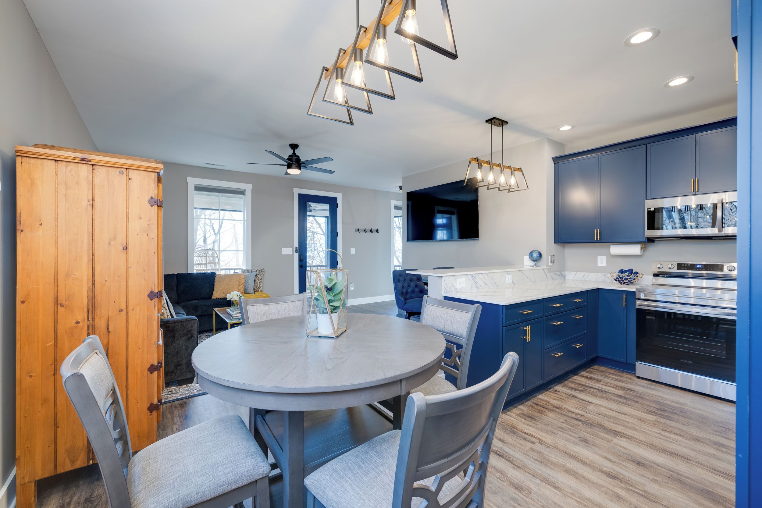A modern kitchen with blue cabinets, a dining area with a round table, and a ceiling fan.