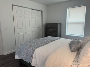 Une chambre à coucher avec un lit, une commode, une fenêtre avec des stores et une porte.