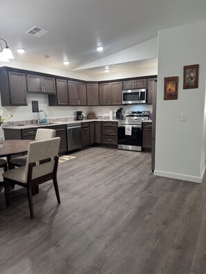 A modern kitchen with dark wood cabinets, stainless steel appliances, and a dining area with a wooden table and chairs.