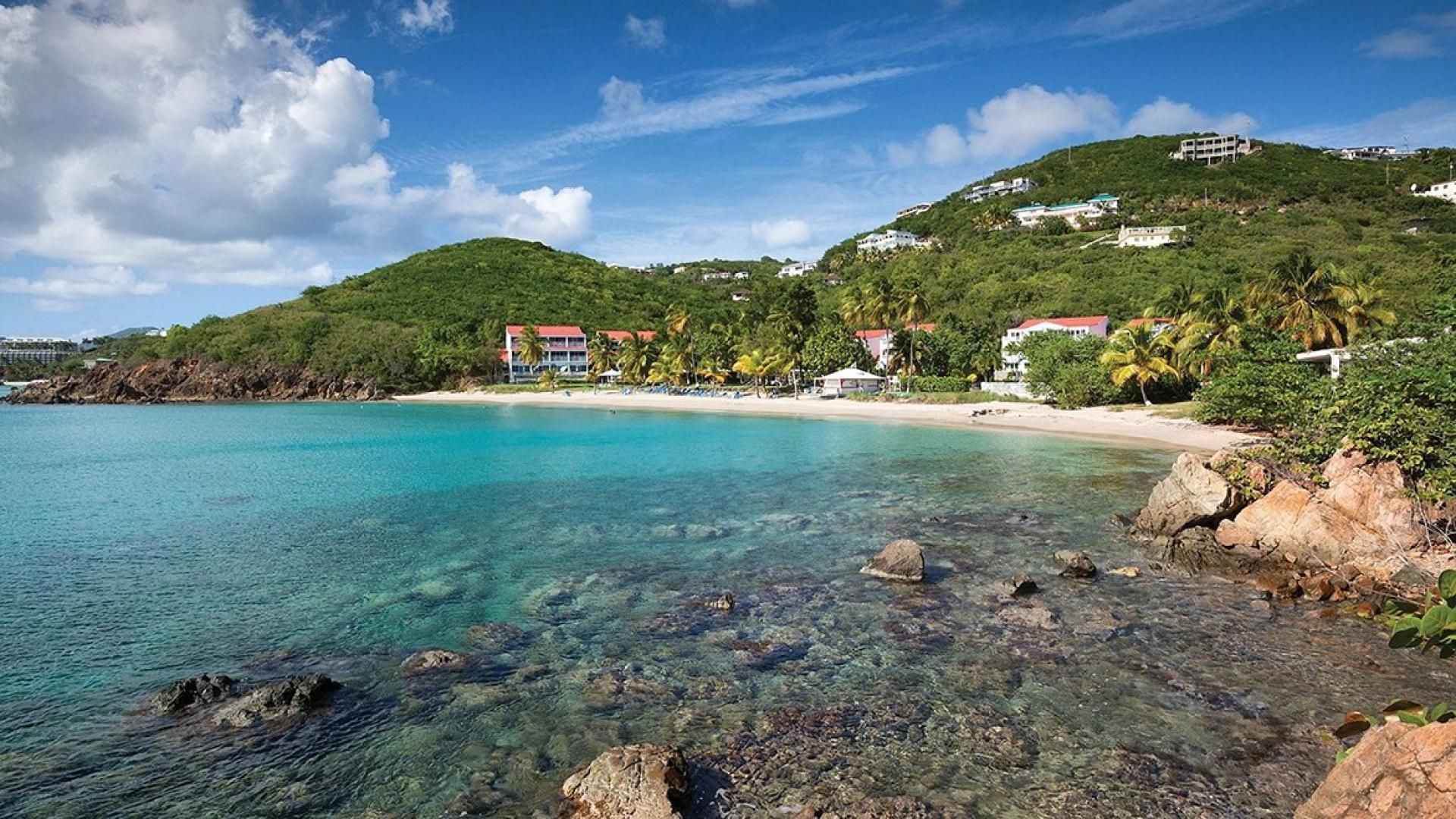 A coastal resort with clear turquoise waters, rocky shoreline, and buildings with red roofs on a hillside.