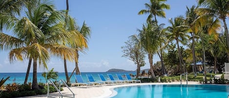 Ett poolområde med solstolar och palmer, med utsikt över en strand.