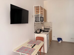 A compact kitchen with a built-in oven, a microwave, and a sink. There is a dining table with a patterned tablecloth and a remote control on it. - WALK37 Syracuse - Between the Greek Theater and Ortigia (Siracusa)