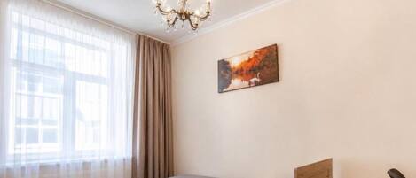Une chambre à coucher avec un lit, une table de chevet, une chaise, une fenêtre avec des rideaux et un tableau au mur.
