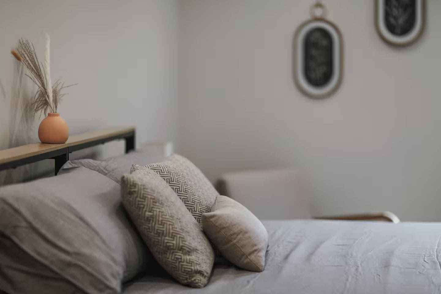 Ein Bett mit zwei Kissen, einer Vase und einer Wand mit zwei gerahmten Bildern.