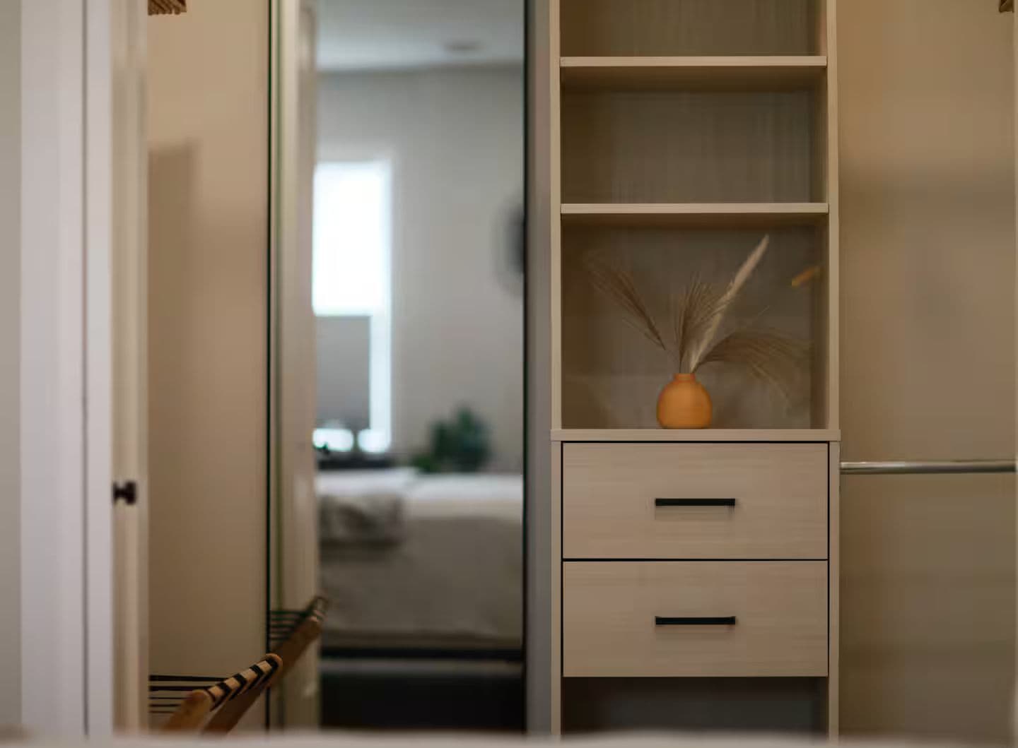 A hallway with a wooden wardrobe, a small table with a vase, and a bed in the background.