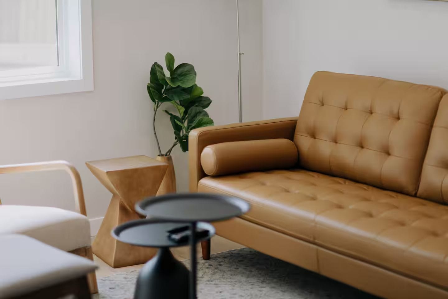 Un salon moderne avec un canapé en cuir marron, une petite table ronde, une table d’appoint en bois et une plante en pot.