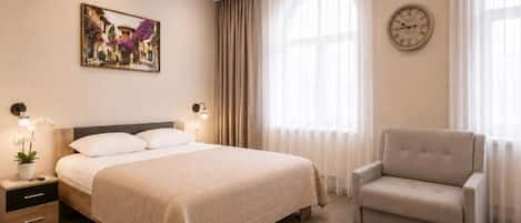 Une chambre d’hôtel avec un lit, une chaise, un tableau, une horloge et une fenêtre avec des rideaux.